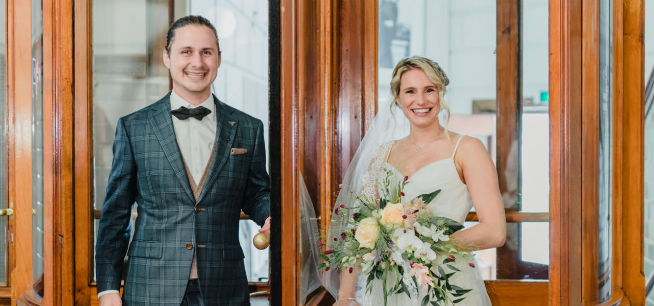 Koppel in pak en witte jurk met een groot boeket., staan in de draaideur bij Hotel New York