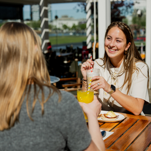 2 vrouwen lachen naar elkaar en zijn aan het genieten van ontbijt en drankjes